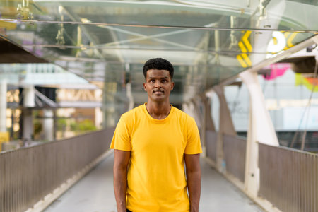 Portrait of handsome black African man wearing yellow t-shirt outdoors in city in Bangkok, Thailandの写真素材