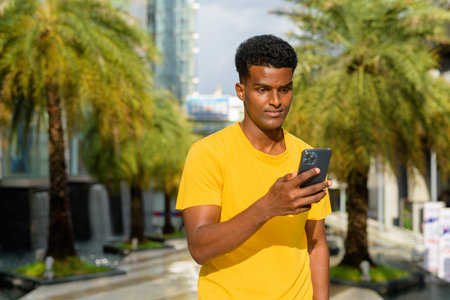 Portrait of handsome black African man wearing yellow t-shirt outdoors in city in Bangkok, Thailand