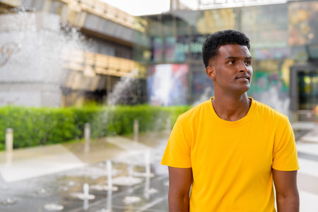 Portrait of handsome black African man wearing yellow t-shirt outdoors in city in Bangkok, Thailandの写真素材