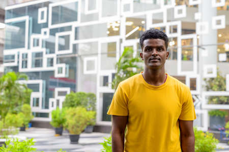 Portrait of handsome black African man wearing yellow t-shirt outdoors in city in Bangkok, Thailandの写真素材