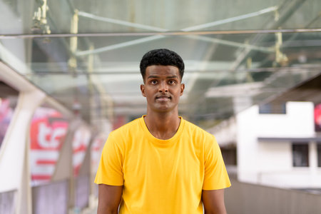 Portrait of handsome black African man wearing yellow t-shirt outdoors in city in Bangkok, Thailand