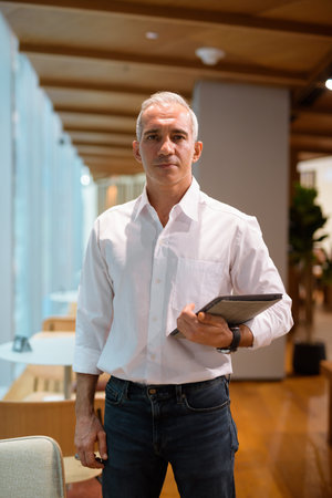 Portrait of handsome businessman holding digital tablet at coffee shop vertical shot