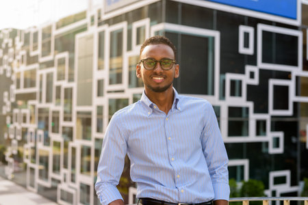 Portrait of handsome black African businessman smiling outdoors in city during summer