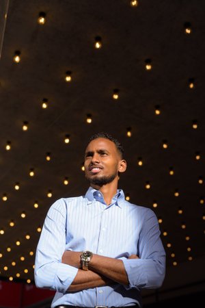 Low angle view shot of handsome black African businessman outdoors in city during summer smiling and thinkingの写真素材