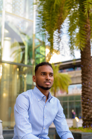 Portrait of handsome black African businessman outdoors in city during summer sitting and thinking...