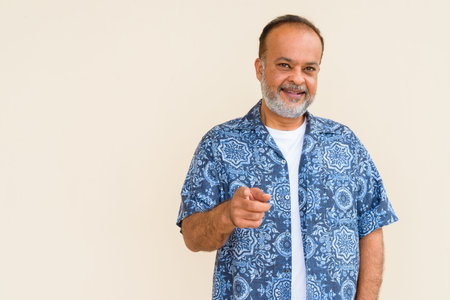 Portrait of handsome Indian man with gray beard against plain wall