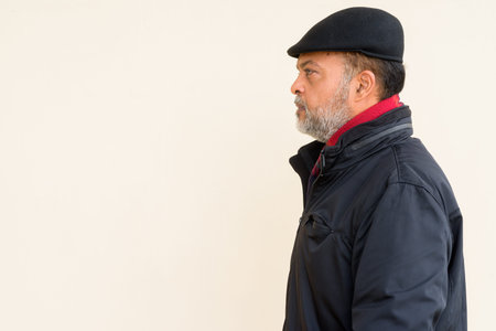 Portrait of handsome Indian man with gray beard against plain wall