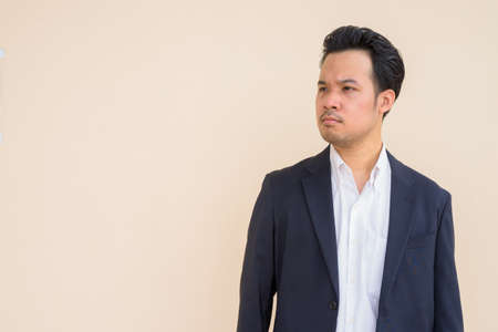 Portrait of Asian businessman wearing suit outdoors against plain backgroundの写真素材