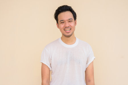 Portrait of Asian man wearing casual white t-shirt against plain background outdoorsの写真素材
