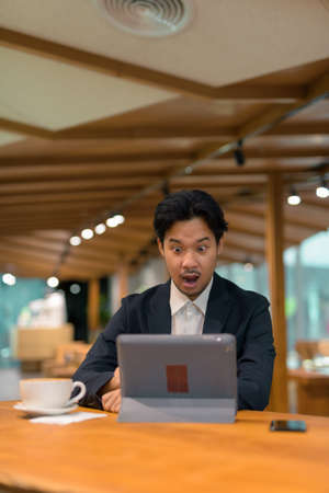 Portrait of Asian businessman sitting in coffee shop using digital tablet computerの写真素材