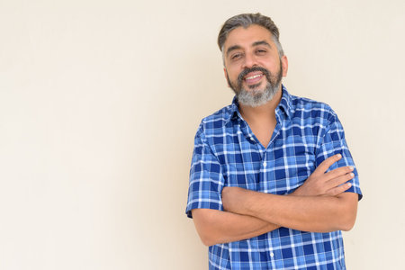 Portrait of handsome bearded Indian businessman against plain background