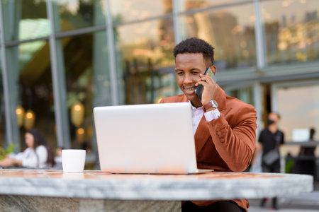 Portrait of African businessman outdoors in coffee shop using laptop computerの写真素材