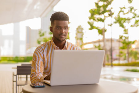Portrait of young handsome African businessman using laptop computer at coffee shop