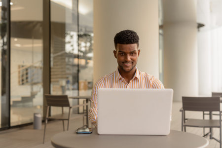 Portrait of young handsome African businessman using laptop computer at coffee shop