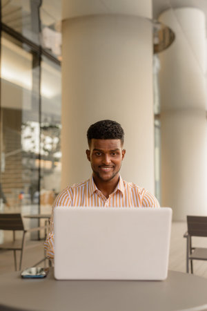 Portrait of young handsome African businessman using laptop computer at coffee shop