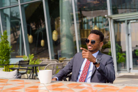 Portrait of African businessman wearing suit and tie in coffee shop outdoors during summerの写真素材