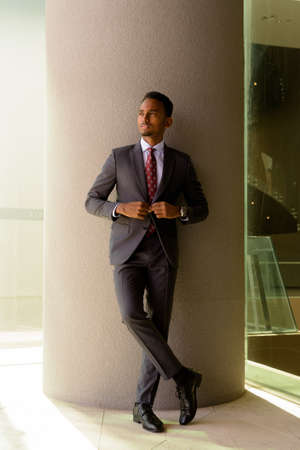 Full length shot of African businessman wearing suit and tie outdoors in city while thinkingの写真素材