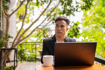 Portrait of handsome young businessman using laptop in coffee shopの写真素材