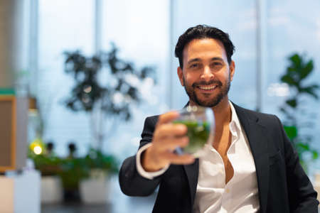 Happy handsome Hispanic businessman at coffee shop having green teaの写真素材