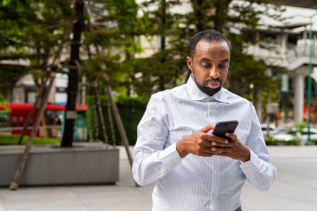 Portrait of handsome black man in city using phone and textingの写真素材