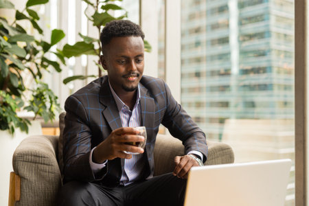 Portrait of African businessman sitting in coffee shop using laptop computerの写真素材