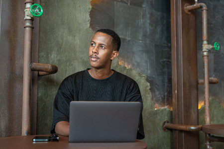 Portrait of handsome black man sitting and using laptop computer indoors