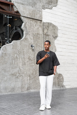 Full body portrait of handsome young African man using phone outdoors