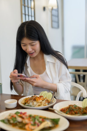 At a restaurant, a young woman happily takes a picture with her phone, embracing her modern lifestyleの写真素材