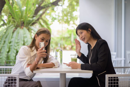 Two Asian women having a pleasant conversation over coffee in a modern cafe setting with greenery...