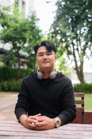 Portrait of Handsome Young Asian Man Sitting Outdoors in Park Concept