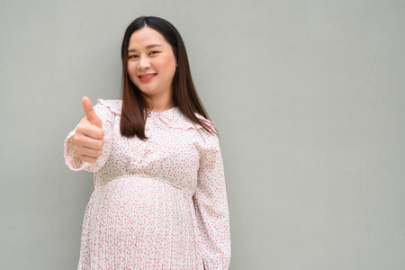 Pregnant Asian woman portrait against plain wallの写真素材