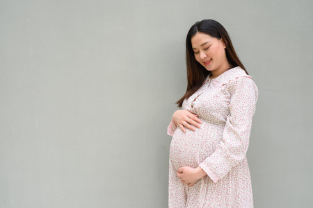 Pregnant Asian woman portrait against plain wallの写真素材