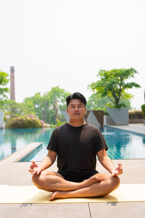 Young Asian man doing yoga exercise next to swimming pool during summerの写真素材