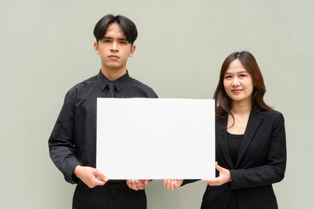 Portrait of young Asian couple wearing business uniform against plain backgroundの写真素材