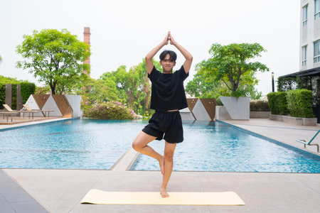 Young man doing yoga outdoors next to swimming pool during summerの写真素材