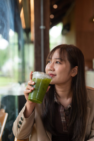 young Asian woman drinking green detox juice in cafeの写真素材
