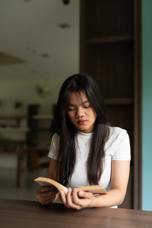 Young beautiful Asian woman reading book in library