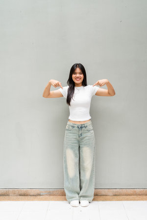 Full length portrait of Asian woman outdoors against plain wall background vertical shotの写真素材