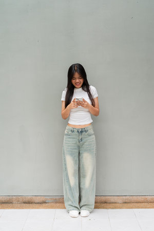 Full length portrait of Asian woman outdoors against plain wall background vertical shotの写真素材