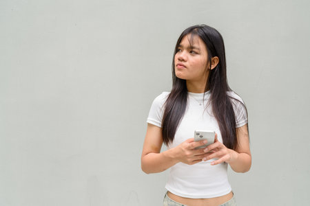 Portrait of beautiful young Asian woman against plain wall backgroundの写真素材