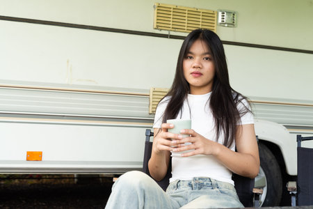 Young woman sitting outside of motorhome RV vehicle in camping siteの写真素材