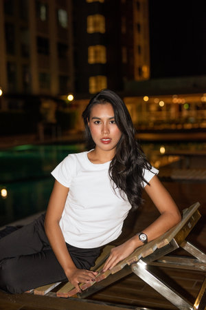 Portrait of young beautiful Asian fashion model posing next to swimming pool during nightの写真素材