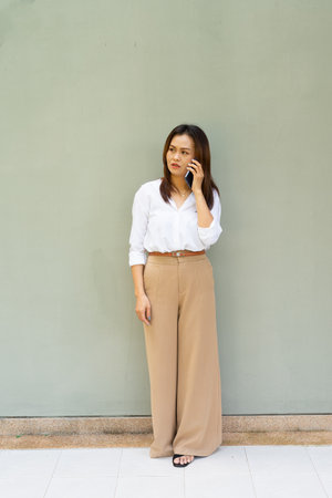 Full length portrait of woman wearing business clothes against plain wall using phoneの写真素材