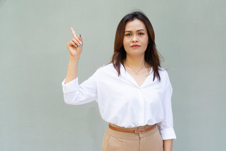Portrait of beautiful Asian businesswoman against plain wall background pointing fingerの写真素材