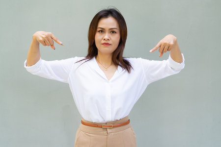 Portrait of beautiful Asian businesswoman against plain wall background pointing fingerの写真素材