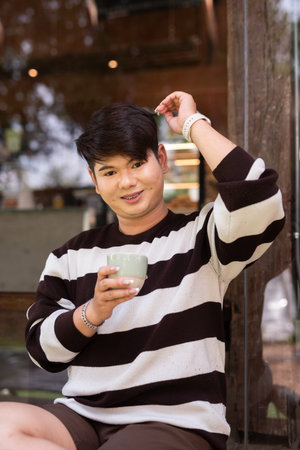 Young cute gay man sitting outdoors in cafe restaurant during day