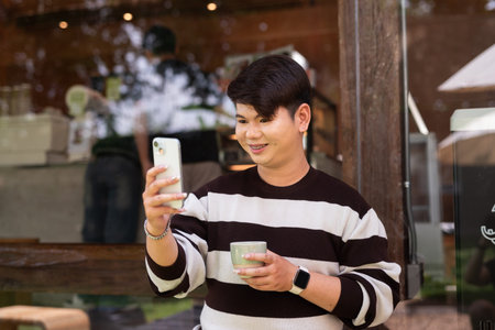 Young cute gay man sitting outdoors in cafe restaurant during day