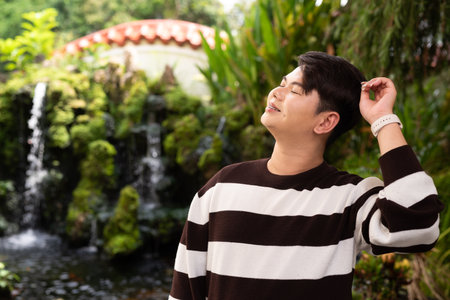 Young cute gay man in Zen style garden park with waterfall relaxing during dayの写真素材