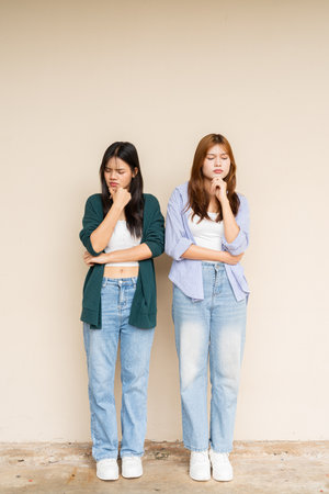 Full length shot of two young Asian woman against plain wallの写真素材