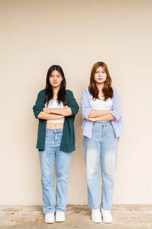 Full length shot of two young Asian woman against plain wallの写真素材